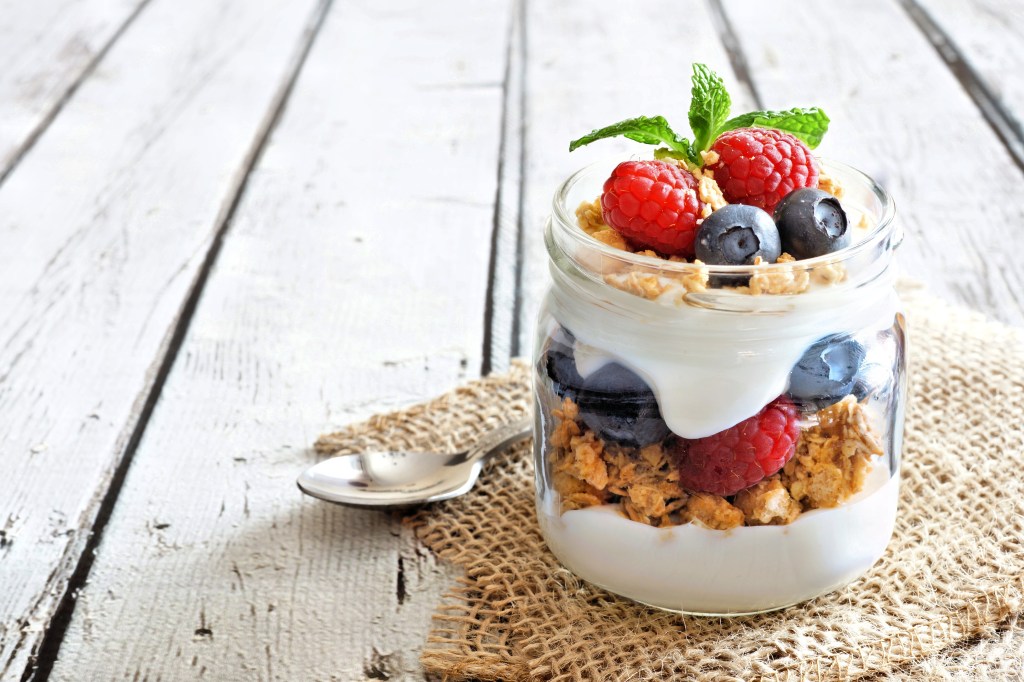 Healthy blueberry and raspberry parfait in a mason jar on a rustic white wood background