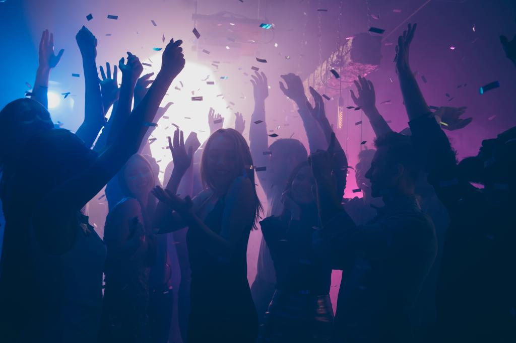 Close up photo of many party people dancing purple lights confetti, flying everywhere nightclub event hands raised up wear shiny clothes
