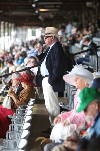 A man wearing a hat and sunglasses stands in the grand stand to watch  the horse race