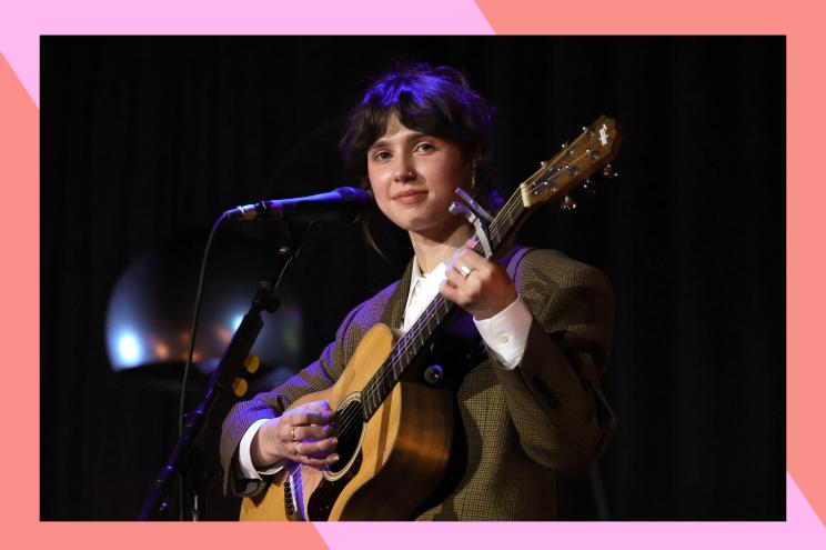 Clairo plays guitar and smiles.