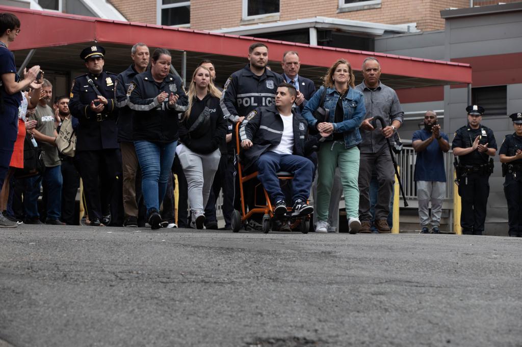 New York City police officers applaud as Officer Richard Yarusso, (center), pushes his partner Officer Christopher Abreu as they leave Elmhurst Hospital in Queens, Monday, June 3, 2024. 