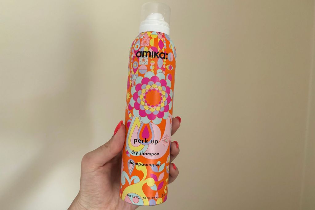 A hand holding a can of dry shampoo.