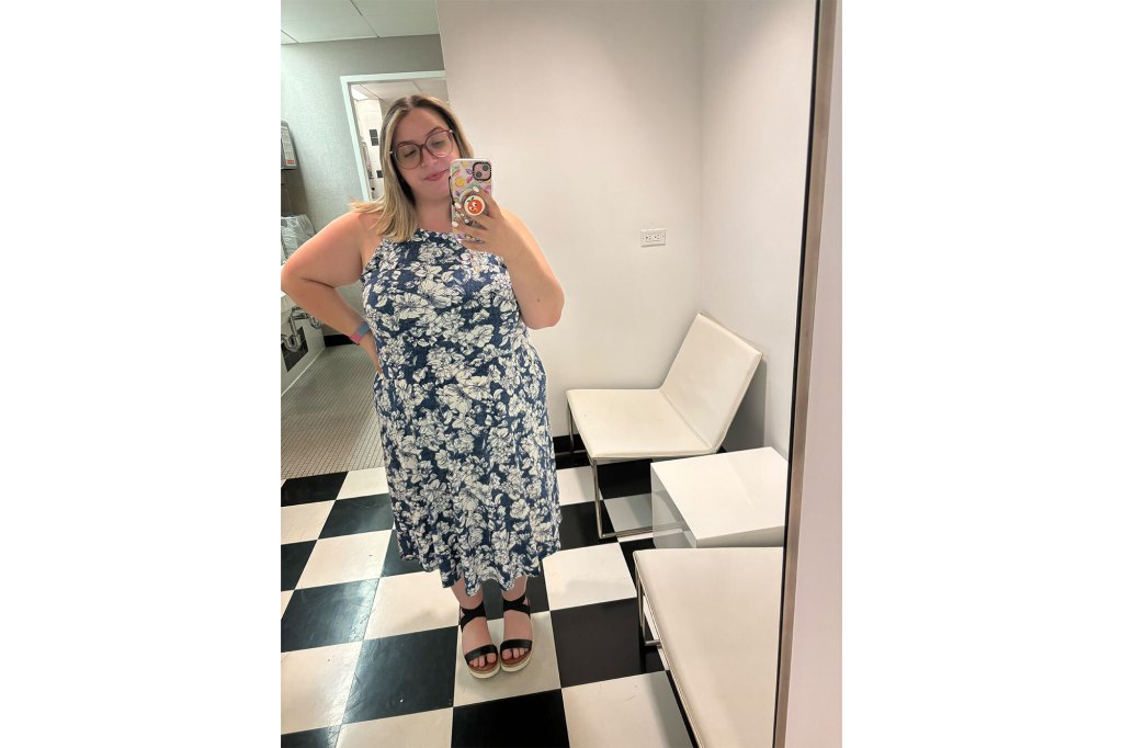 A woman in a white and blue printed dress, taking a selfie.