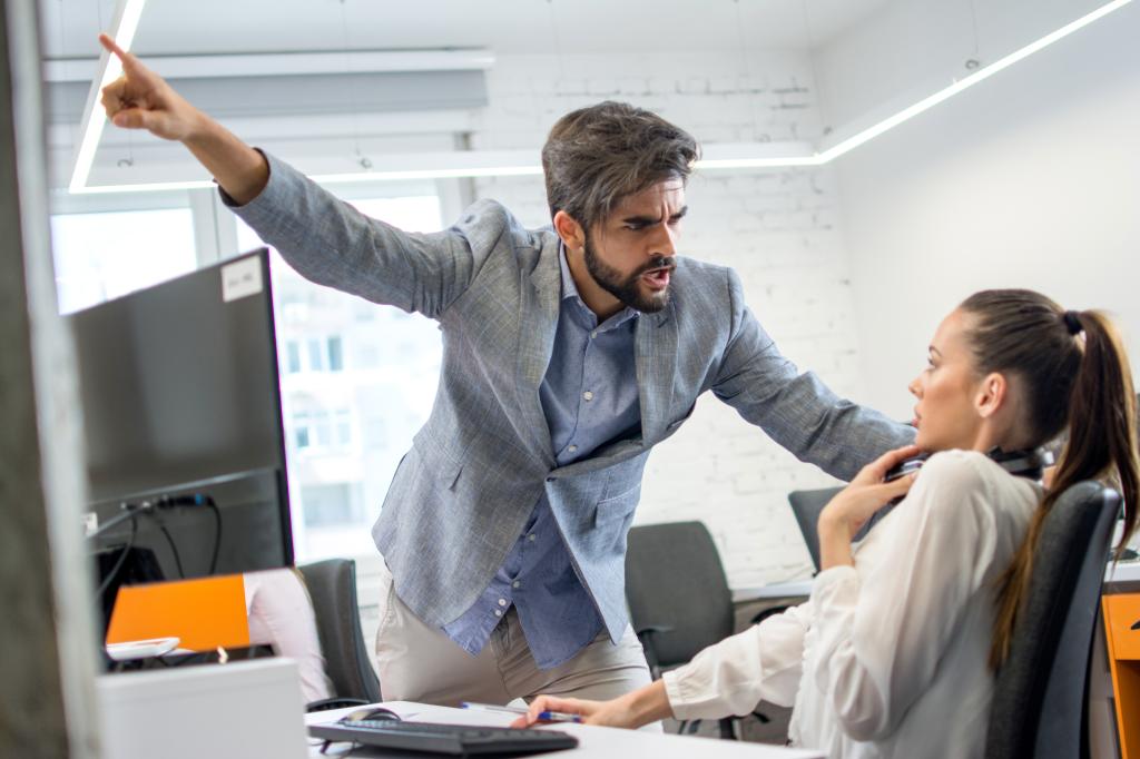 Young male boss angrily pointing at a stressed and scared female employee in office setting, illustrating double standards and microaggressions in the workplace.