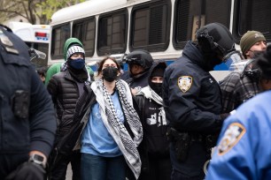 An arrested female student with a keffiyeh and mask waits to get on the NYPD bus.