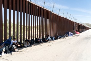 Asylum-seeking migrants from various countries such as India, Colombia, Brazil, and China rest in a shade by the border wall as they wait to be transported at a staging area, after U.S. President Joe Biden announced a sweeping border security enforcement effor