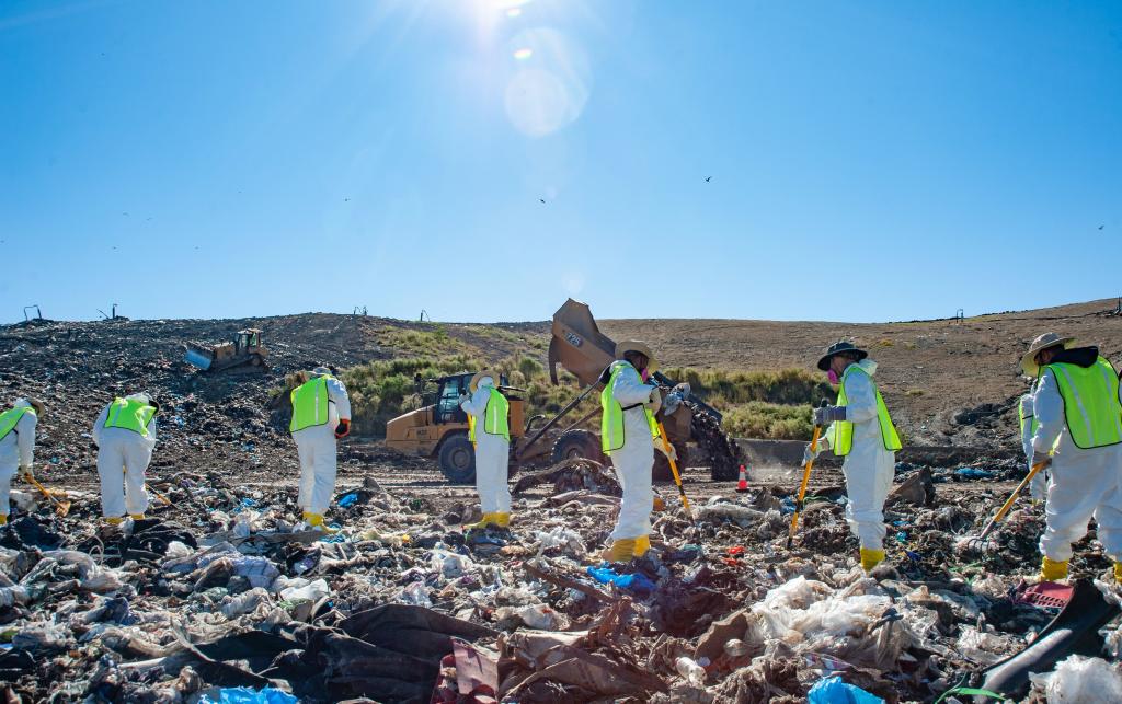 investigators in yellow vests comb through garbage at a landfill