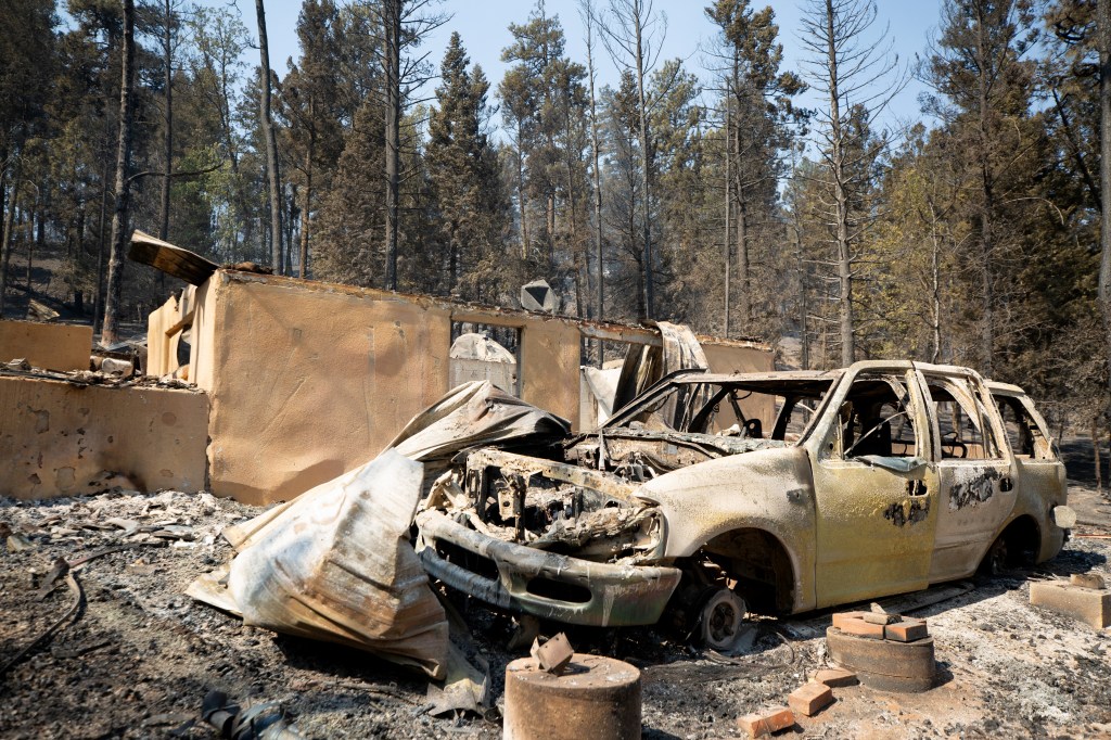 A burned car stands in front of a ruined building as the South Fork Fire burned most of the structures in Cedar Creek.