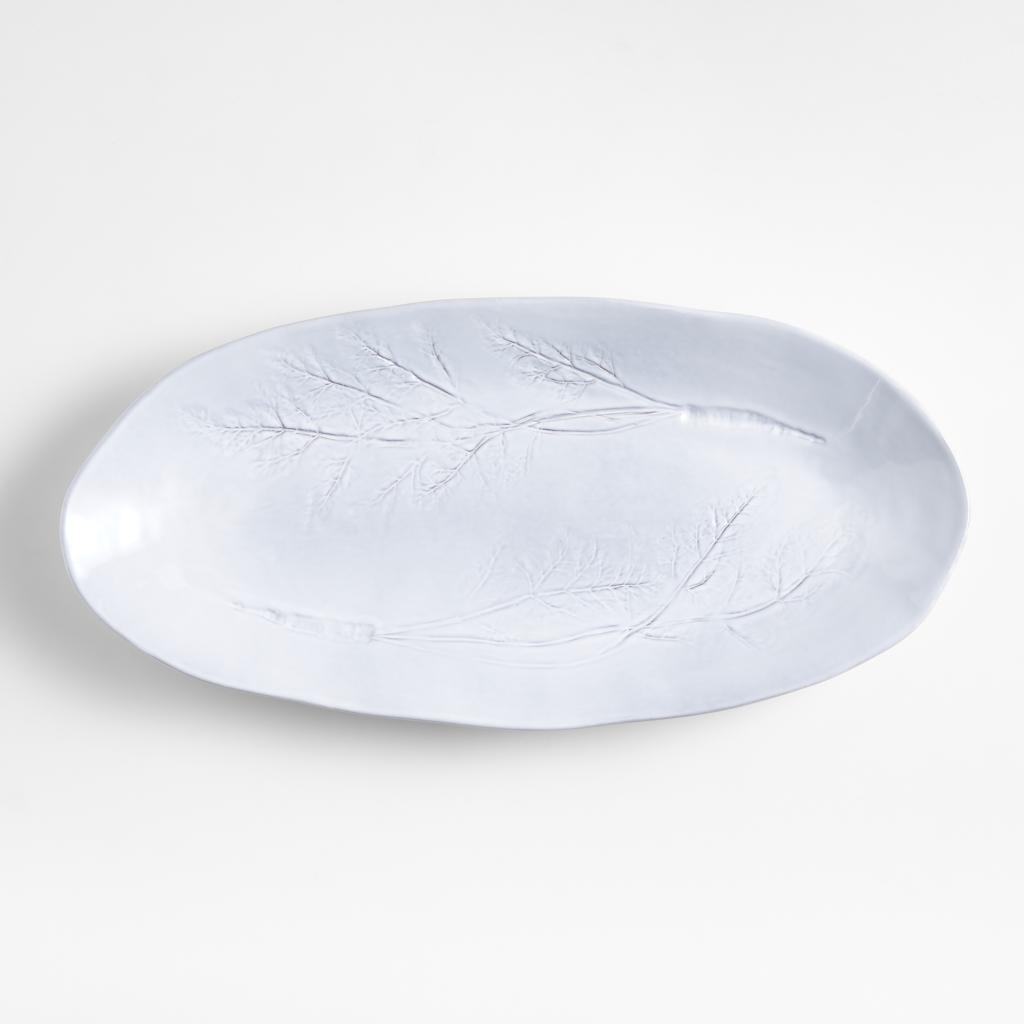 A white oval ceramic serving platter designed by Laura Kim, featuring a tree design.