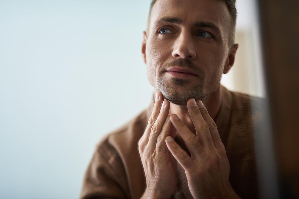 Young man touching his chin while examining his skin condition