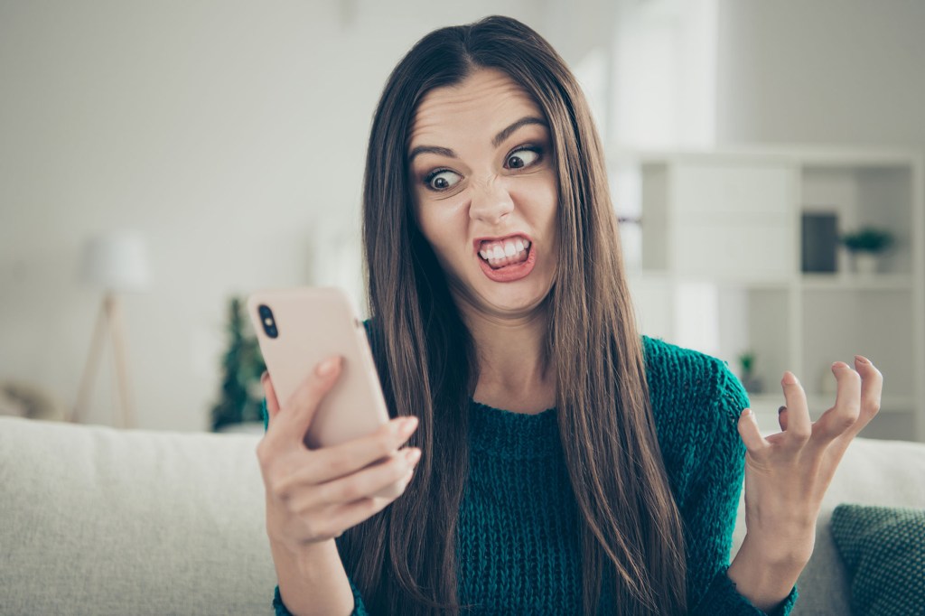 A woman making a funny face, grinning and grimacing, while holding a broken telephone