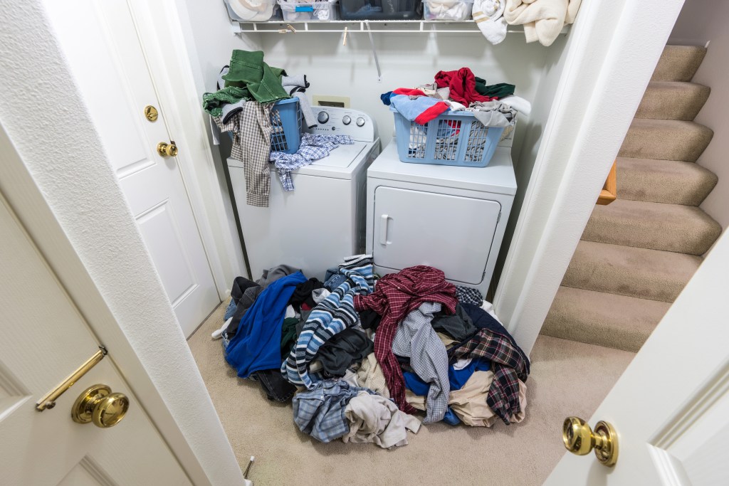 Cluttered laundry room with large piles of unwashed clothes