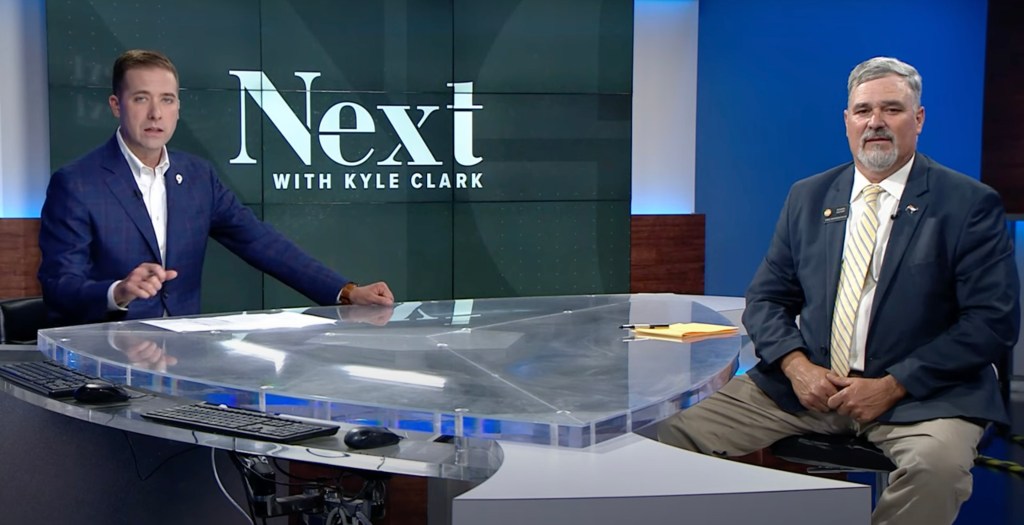Kyle Clark and Richard Holtorf sitting at a desk on a TV set.