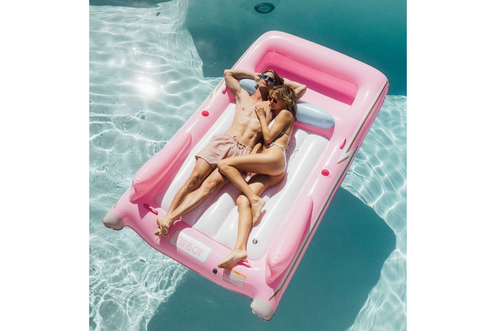 A man and woman lying on a pink raft in a pool