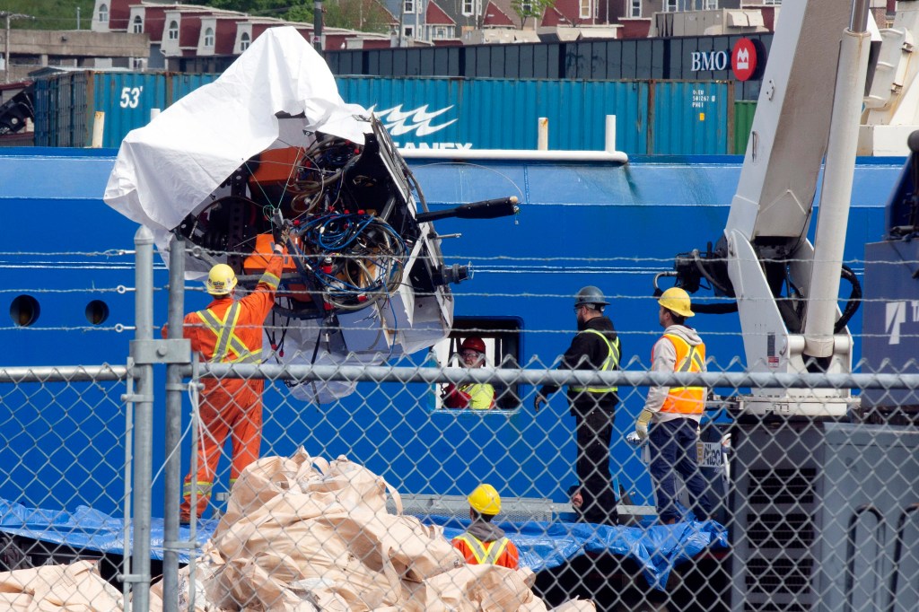 Workers in safety vests unloading debris from the Titan submersible, recovered from near the Titanic wreck, from the ship Horizon Arctic at a Canadian Coast Guard pier.