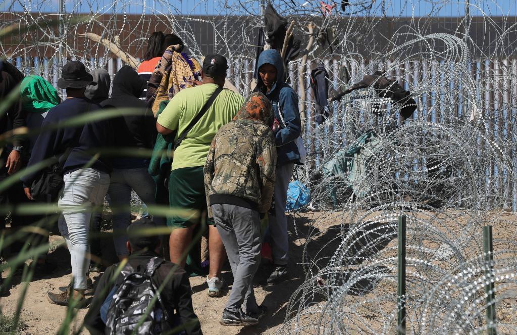 Migrants wait between barbed wire near the border wall in El Paso, Texas.