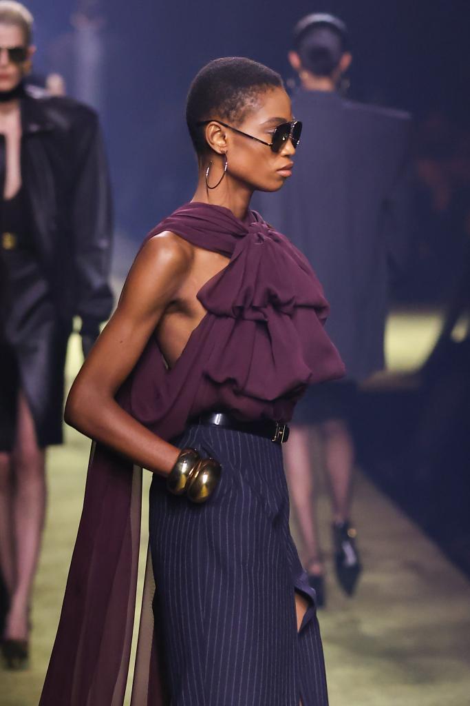 A model wearing sunglasses and a purple shirt walking on the runway during Saint Laurent Womenswear Fall Winter 2023-2024 show for Paris Fashion Week