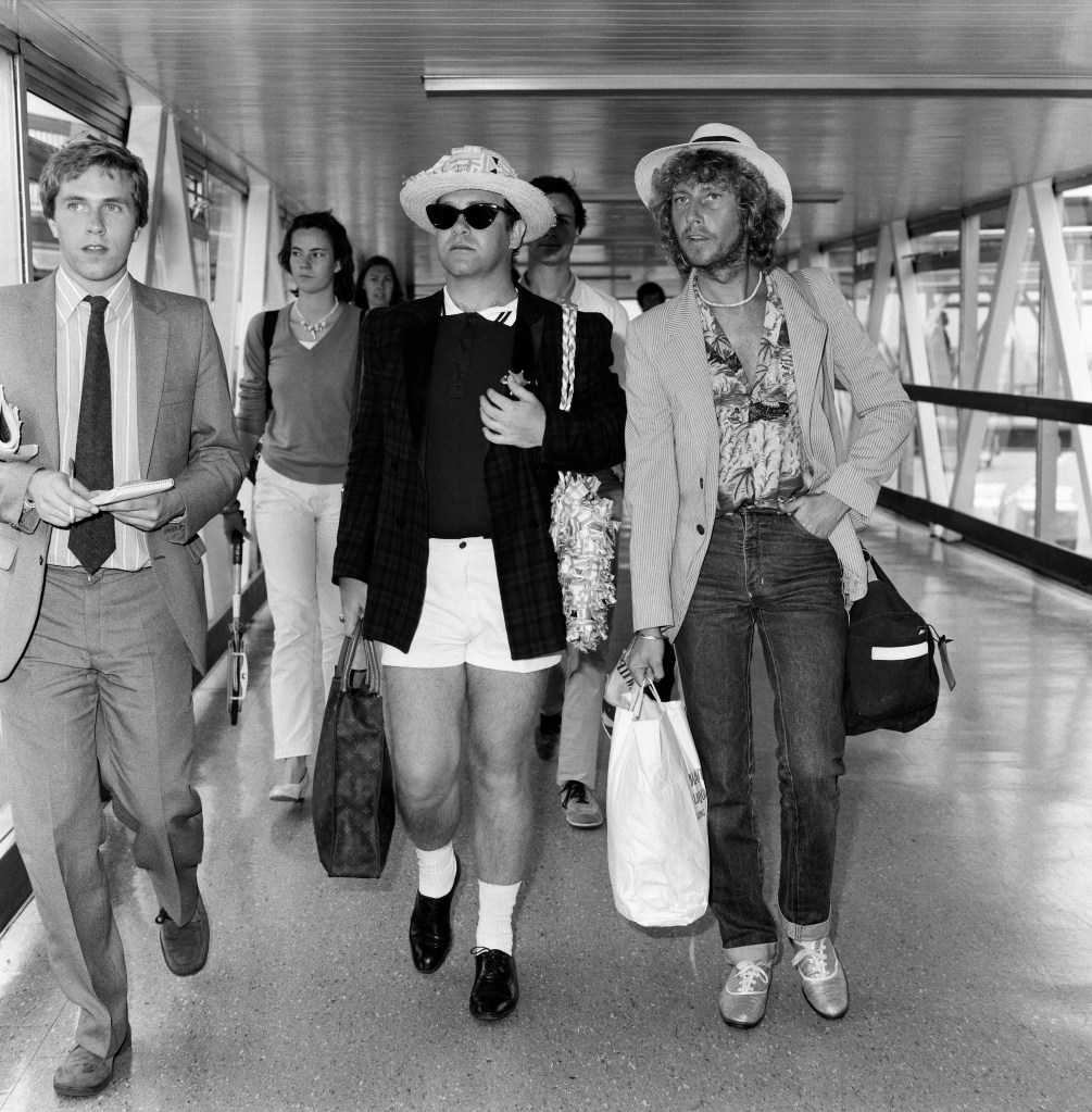 Elton John walking at Heathrow Airport, August 20th, 1981, popularizing shorter in-seams in men's fashion