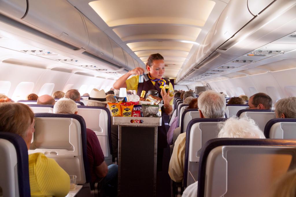 EP0ET1 A flight attendant member of the cabin crew serving food on a Monarch Airlines airplane from Madeira to Gatwick airport, UK