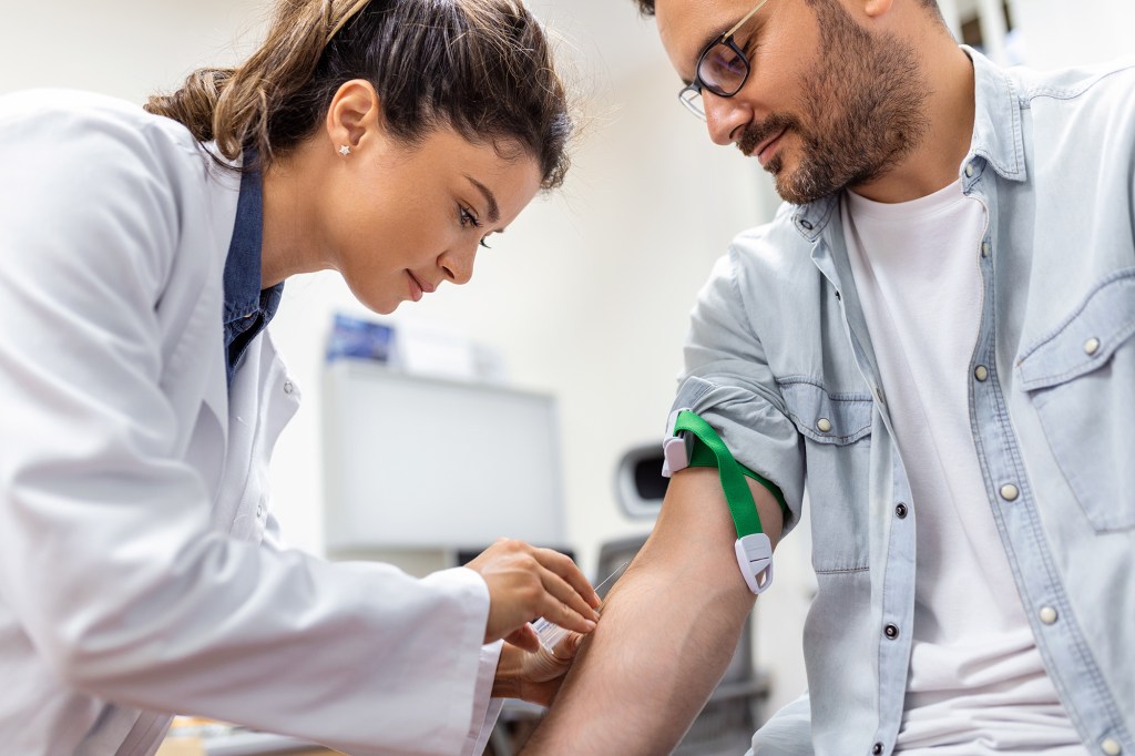 Friendly hospital phlebotomist in medical uniform collecting blood sample from patient in bright white lab room