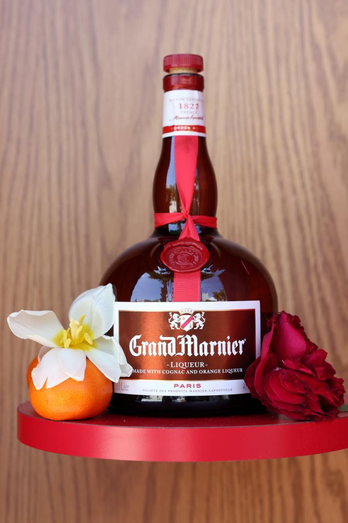 Bottle of Grand Marnier on a red self next to an orange and flowers