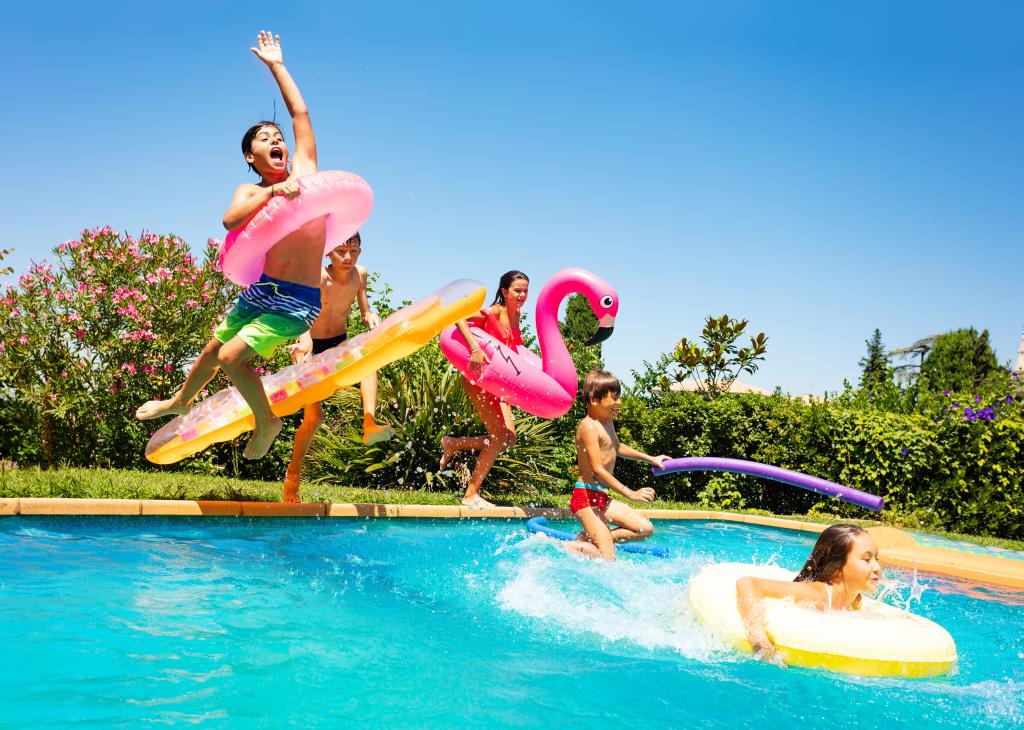 Group of joyful, age-diverse children with swim floats jumping into a pool during vacation