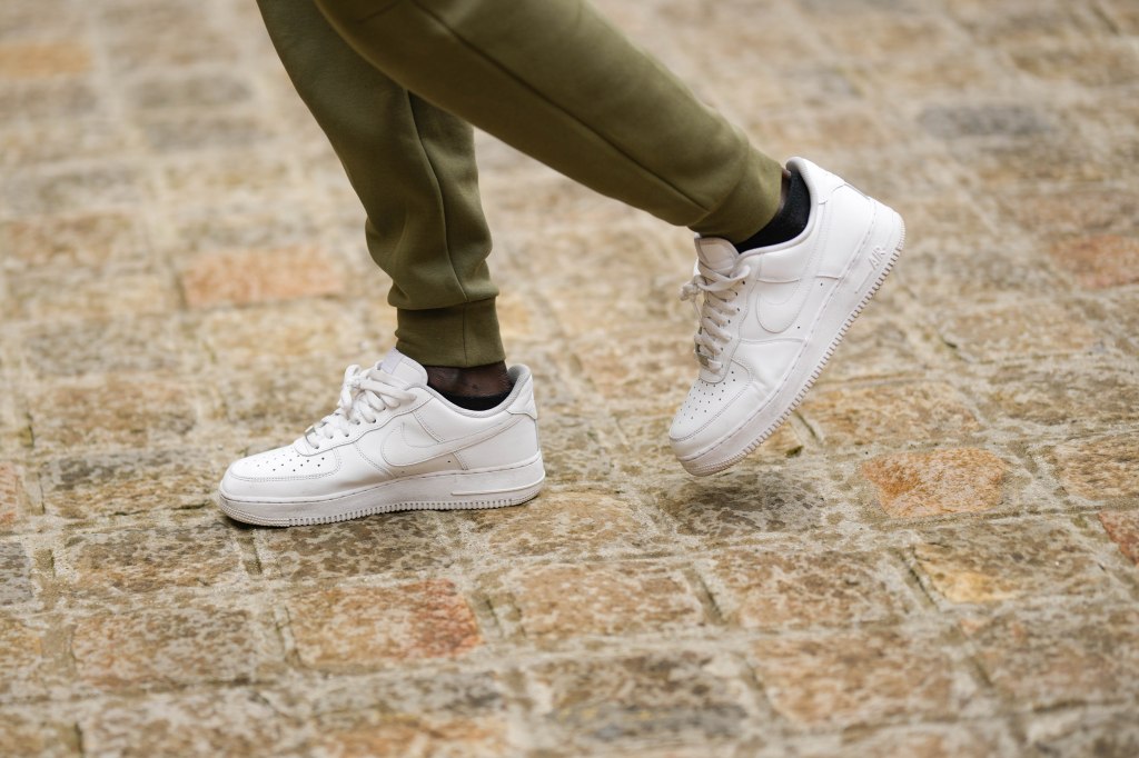 PARIS, FRANCE - APRIL 26: A guest wears green and khaki bicolored pattern sport pants from Nike, white shiny leather laces Air Force One sneakers from Nike, outside the COS show, 