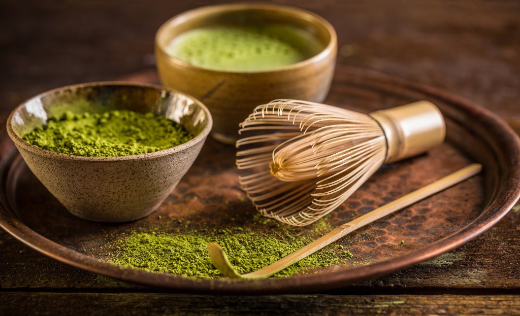 A bowl of green matcha tea with a whisk