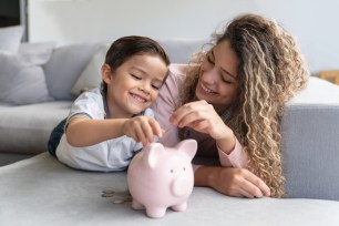 Portrait of a happy mother and son saving money in a piggybank and smiling - home finances concepts