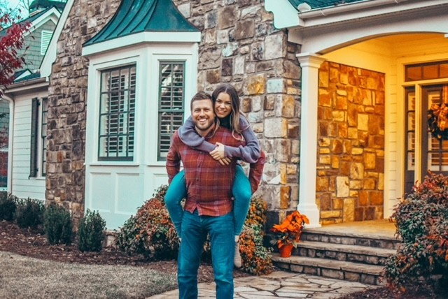 couple smiling outside house, woman piggybacking on man