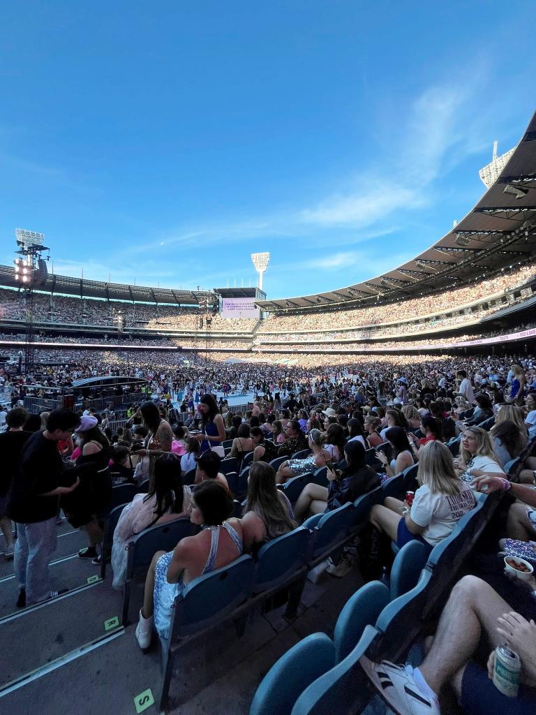 Pregnant woman dancing amidst a large crowd at a Taylor Swift concert in Melbourne, Australia.