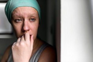 Pensive young Muslim woman with a headscarf, fighting breast cancer, standing next to a hospital window looking out