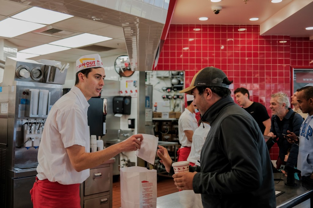 An In-N-Out staff, with the logo prominently displayed his hat, serves a customer.