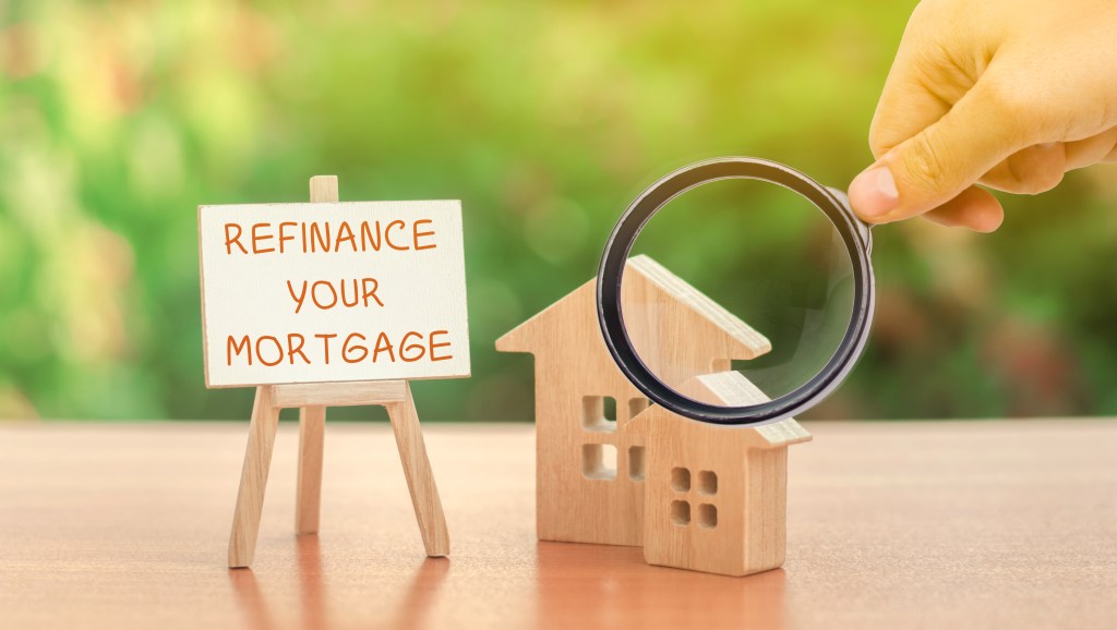 Magnifying glass highlighting the inscription 'Refinance Your Mortgage' near miniature wooden houses, representing real estate financing concepts.