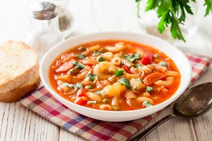 Bowl of Italian minestrone soup with pasta and vegetables on a white wooden background