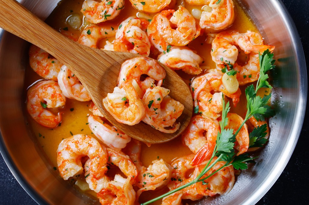 Top view of Italian shrimp scampi with garlic butter sauce, lemon, and parsley in a skillet on a concrete background, close-up