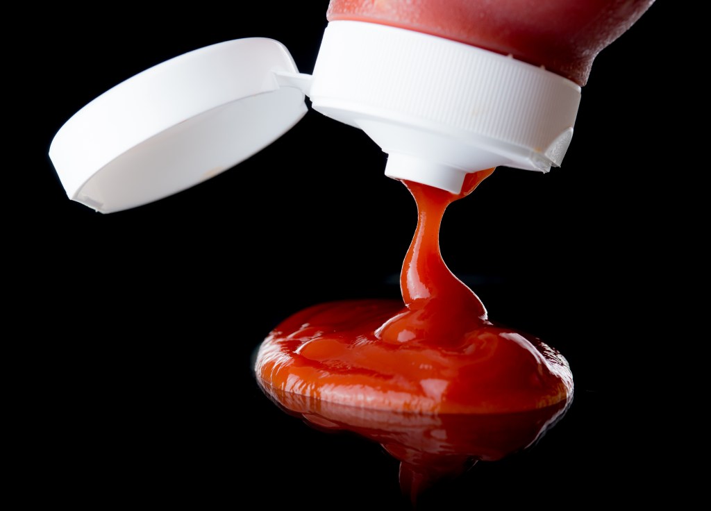 Ketchup or tomato sauce falling from bottle over dark background