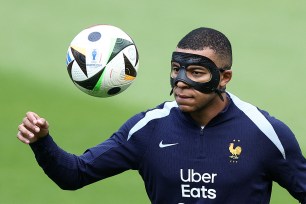 Kylian Mbappé wearing a black mask and holding a football