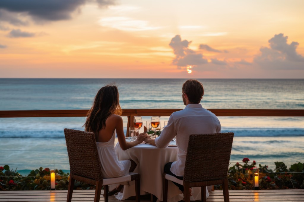 A man and woman enjoying a luxurious dinner on a beach deck with wine glasses