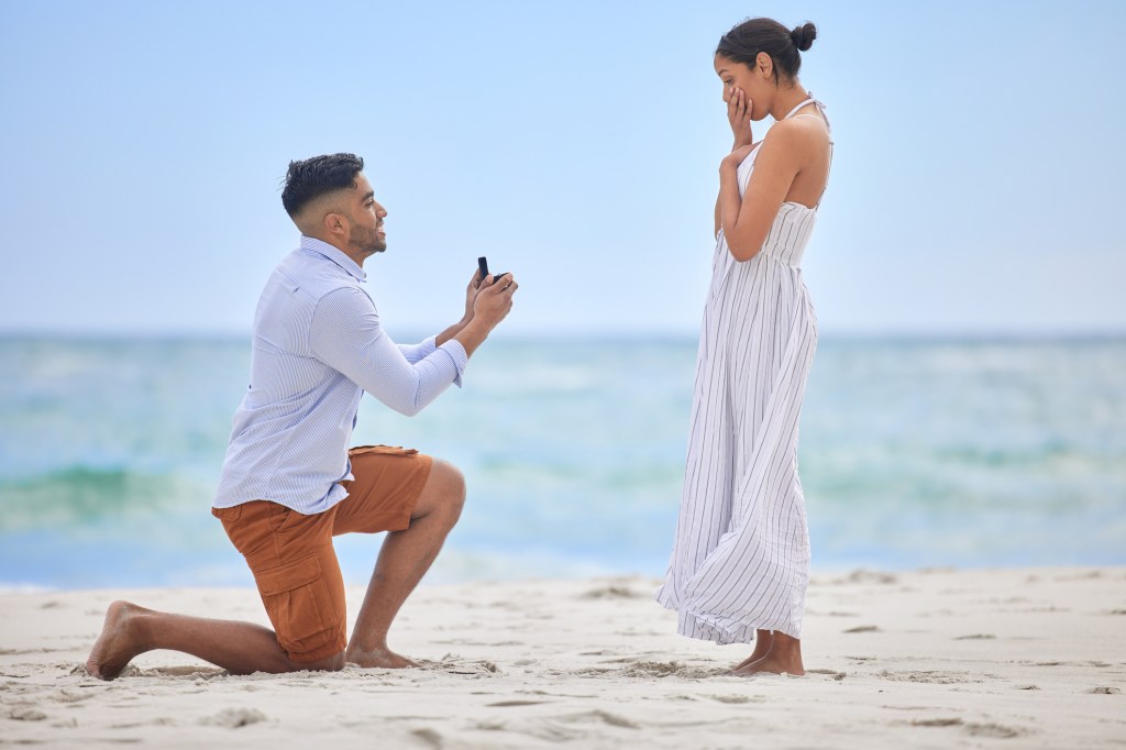 Young man proposing to his girlfriend on a beach during summertime