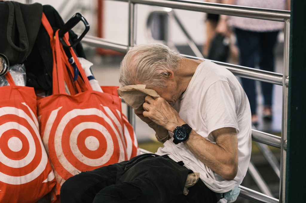 Man dabbing his face with a napkin in Union Square subway station during a hot day