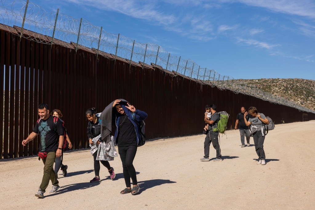 Migrants holding luggage and walking across the U.S. southern border near Jacumba Hot Springs, California.