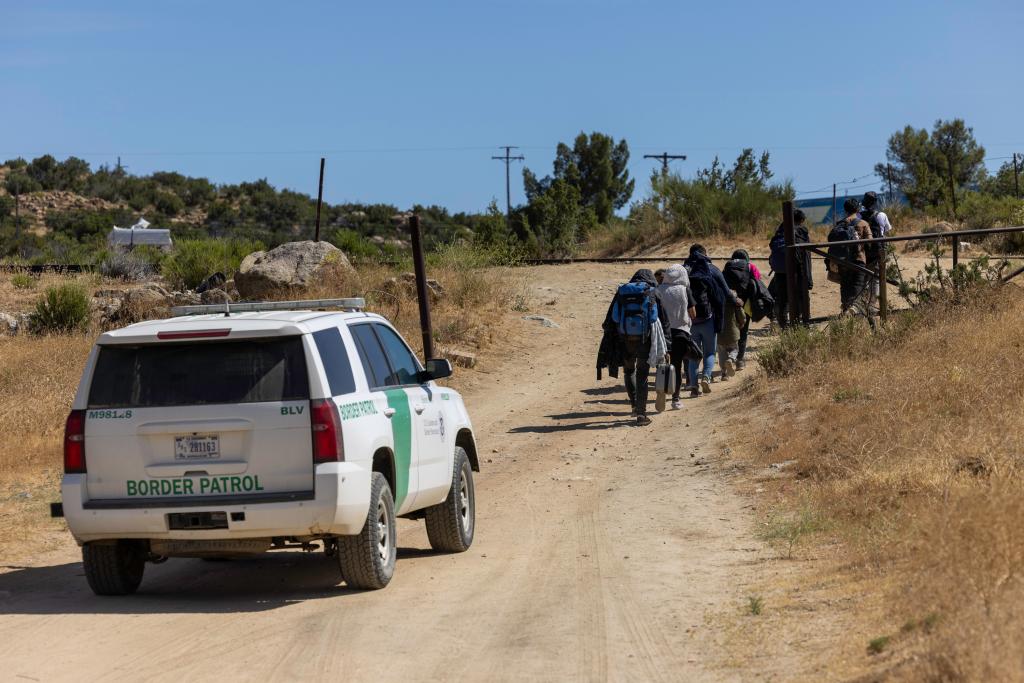 After crossing the border from Mexico, a group of a dozen migrants from Sudan, Mauritania, India, China, Iran and many areas of Latin America walk ahead of a Border Patrol vehicle in a remote area of southern California.