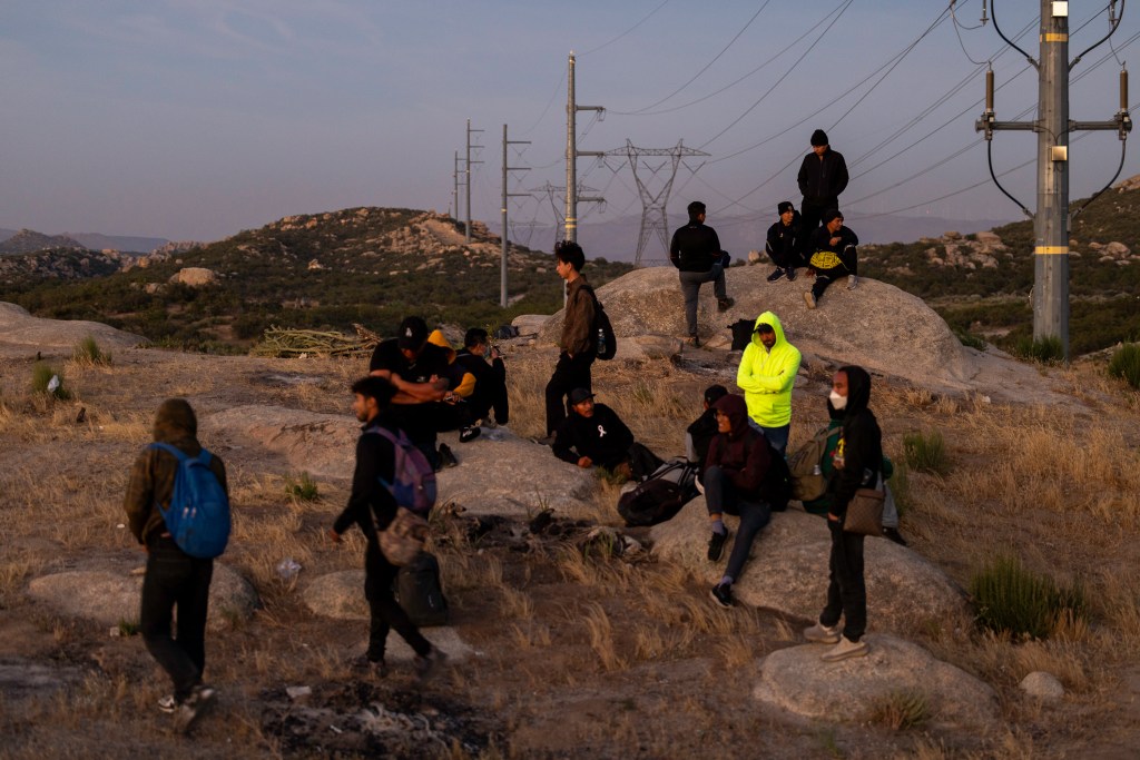 About a dozen migrants stand atop rocks in Jacumba Hot Springs, California, after crossing the border illegally.