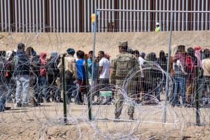 A group of people from Venezuela seeking asylum, standing around barbed wire at Juarez, Mexico