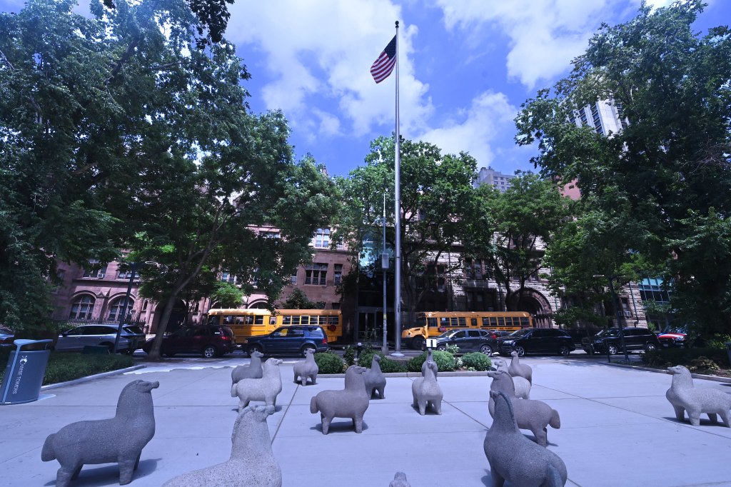 Stone llama statues in Llama Park at the renovated Wise Towers playground, New York City, with Trinity School seen in background, american flag post at center.