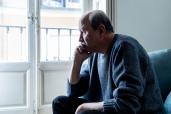 Depressed senior man suffering from Alzheimer's sitting alone on home couch, struggling with feelings of loneliness and confusion