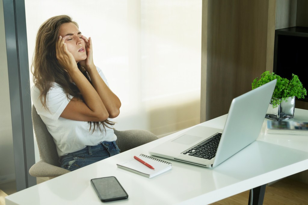 Overworked woman sitting at her office desk with hands on her face, indicating headache