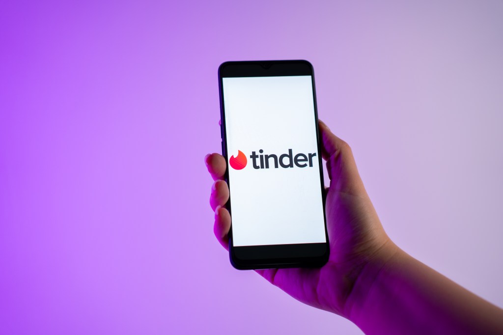 Person in Athens, Greece holding a mobile phone displaying the Tinder dating app logo on the screen