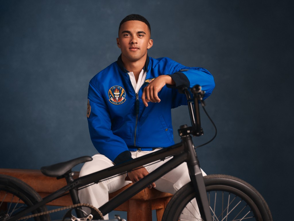 BMX athlete Kamren Larsen sitting on a stool with a bicycle, wearing Ralph Lauren Olympic attire